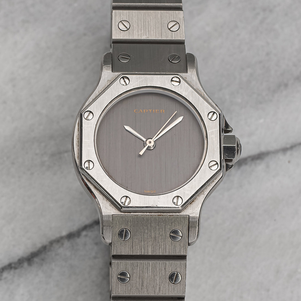 Close view of a lady's steel Santos Octagon with the plain brushed grey 'Ghost' dial bearing only the Cartier signature, steel hands and the screwed octagonal bezel. · Photo: Danny's Vintage Watches · © Danny's Vintage Watches, used with permission · Source: https://dannysvintagewatches.com/products/cartier-octagon-ladies-grey-ghost-dial